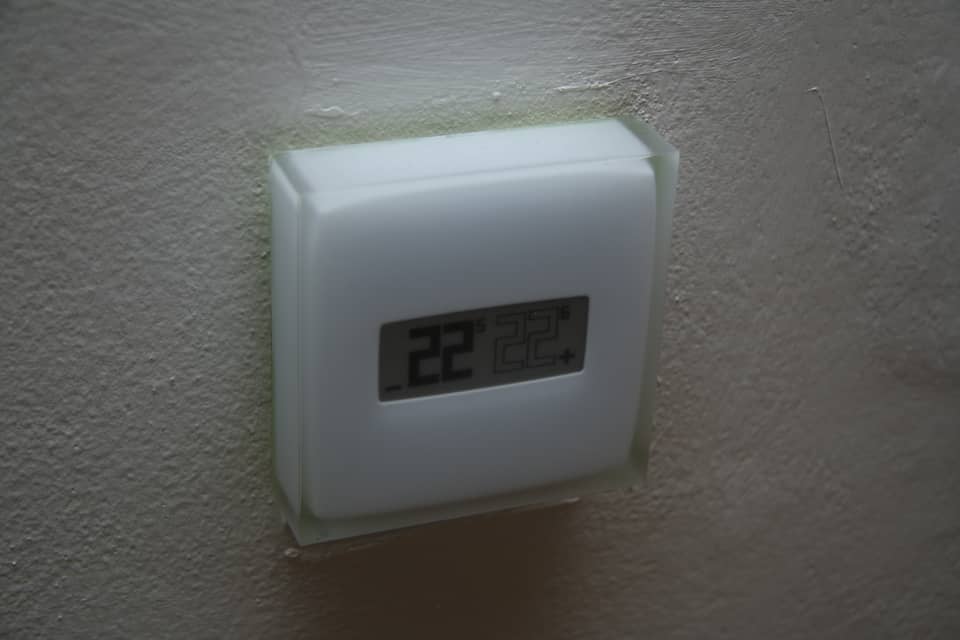 A white Netatmo wall thermostat mounted on a textured painted wall, its display showing 22 degrees.