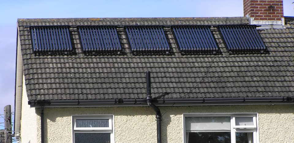 Five evacuated-tube solar water-heating panels in a row on the concrete-tiled roof of a pebble-dashed semi-detached house.